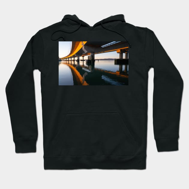 Morning sun strikes side Tauranga Harbour Bridge in golden hue reflected leading lines into calm water below Hoodie by brians101